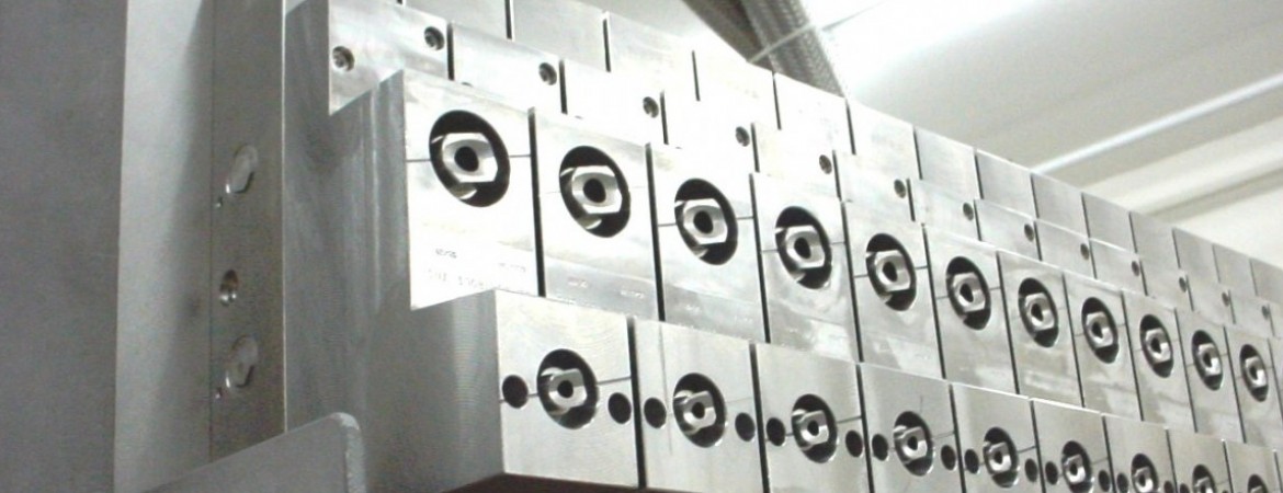 Row of silver metal blocks with circular sockets arranged in a grid on an industrial machine.